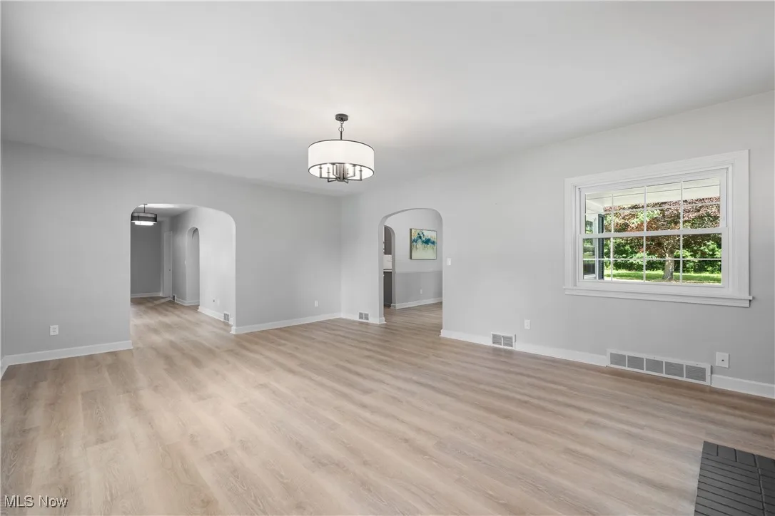 Spare room with arched walkways, a chandelier, and light wood-type flooring