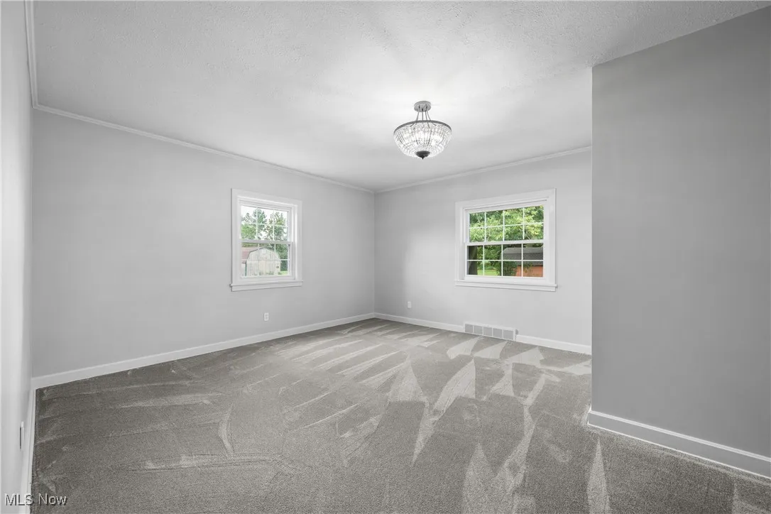 Carpeted empty room with ornamental molding, a chandelier, and a textured ceiling