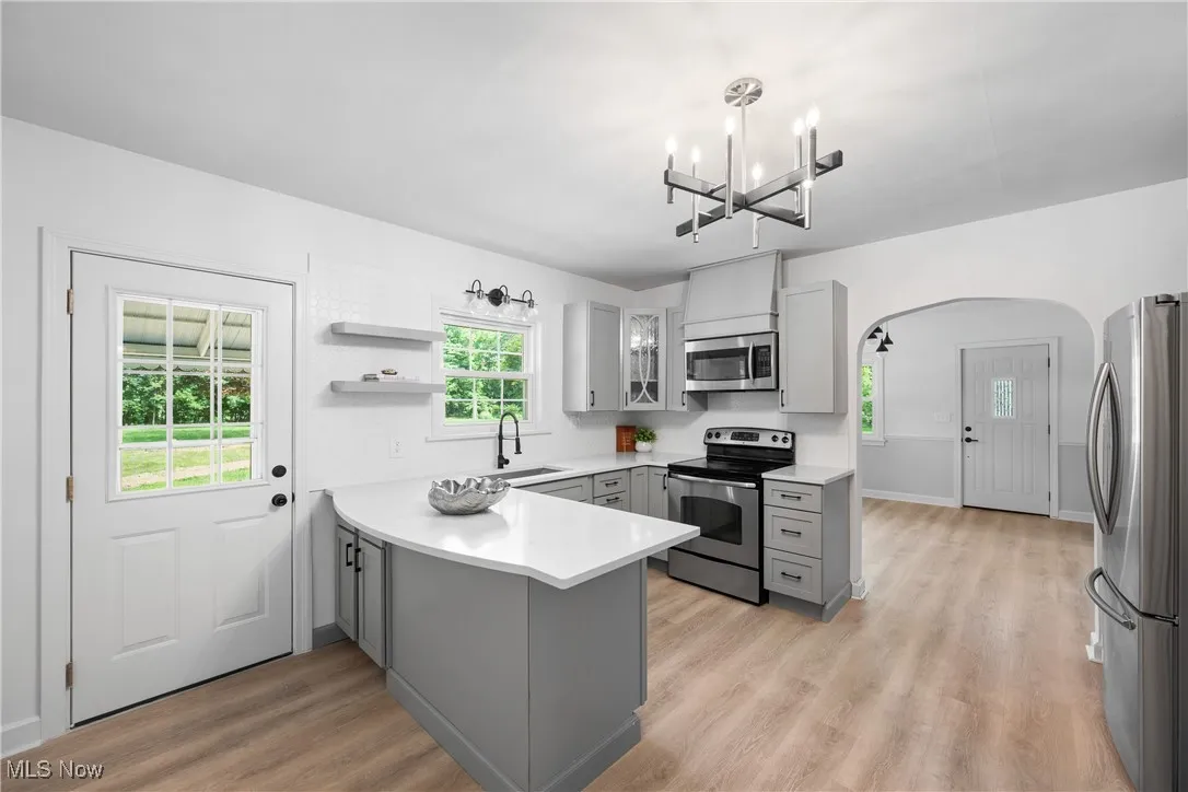 Kitchen featuring gray cabinets, a peninsula, appliances with stainless steel finishes, a chandelier, and arched walkways