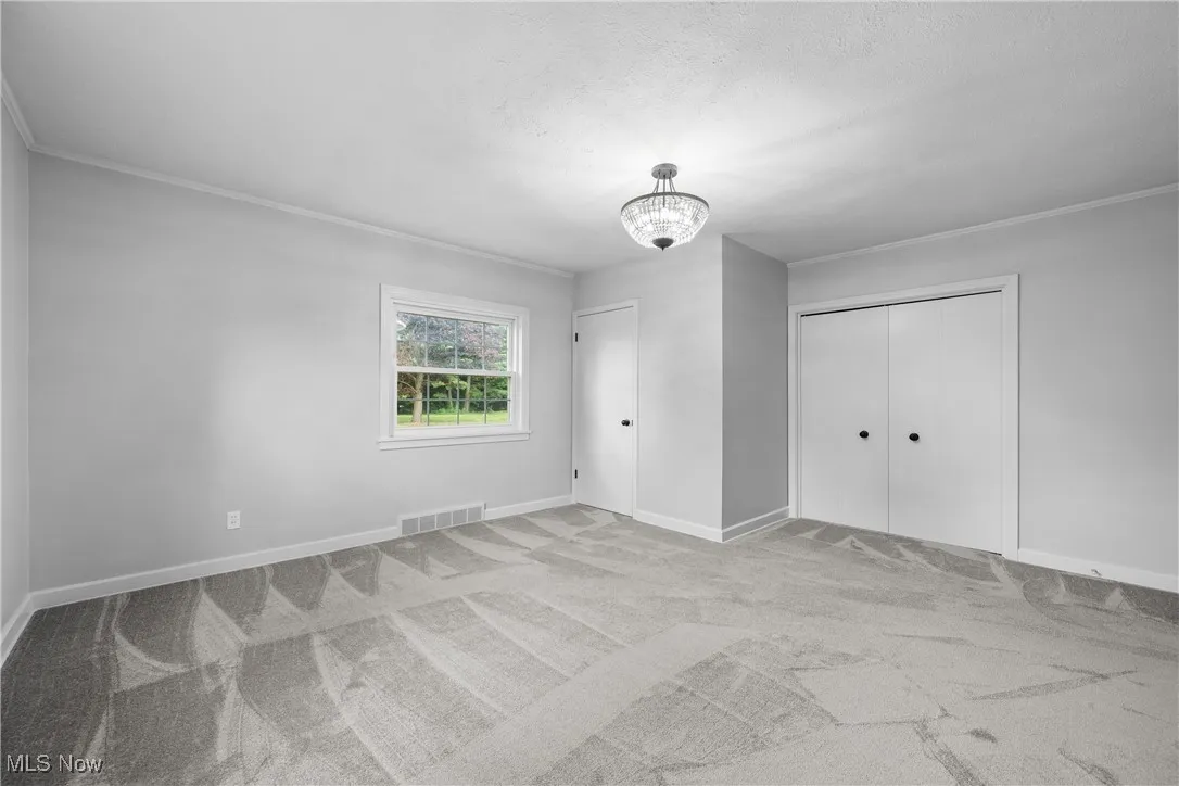 Unfurnished bedroom with crown molding, carpet flooring, a chandelier, and a closet