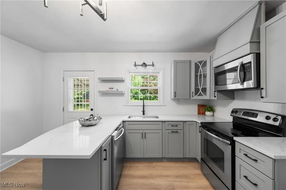 Kitchen with gray cabinetry, appliances with stainless steel finishes, a peninsula, light wood-style flooring, and open shelves