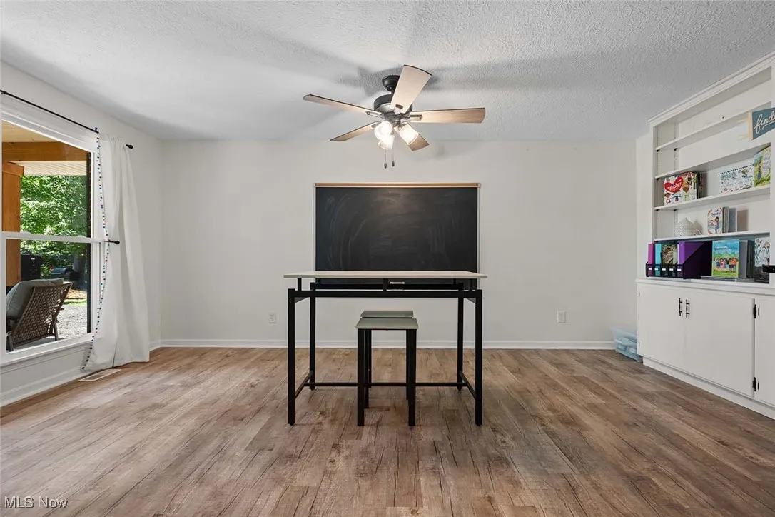 Living area with built in shelves, a textured ceiling, wood finished floors, and a ceiling fan