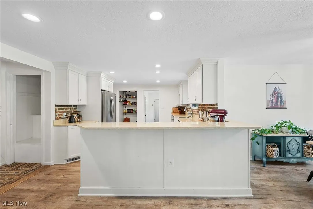Kitchen featuring tasteful backsplash, light countertops, light wood-style floors, white cabinets, and a textured ceiling