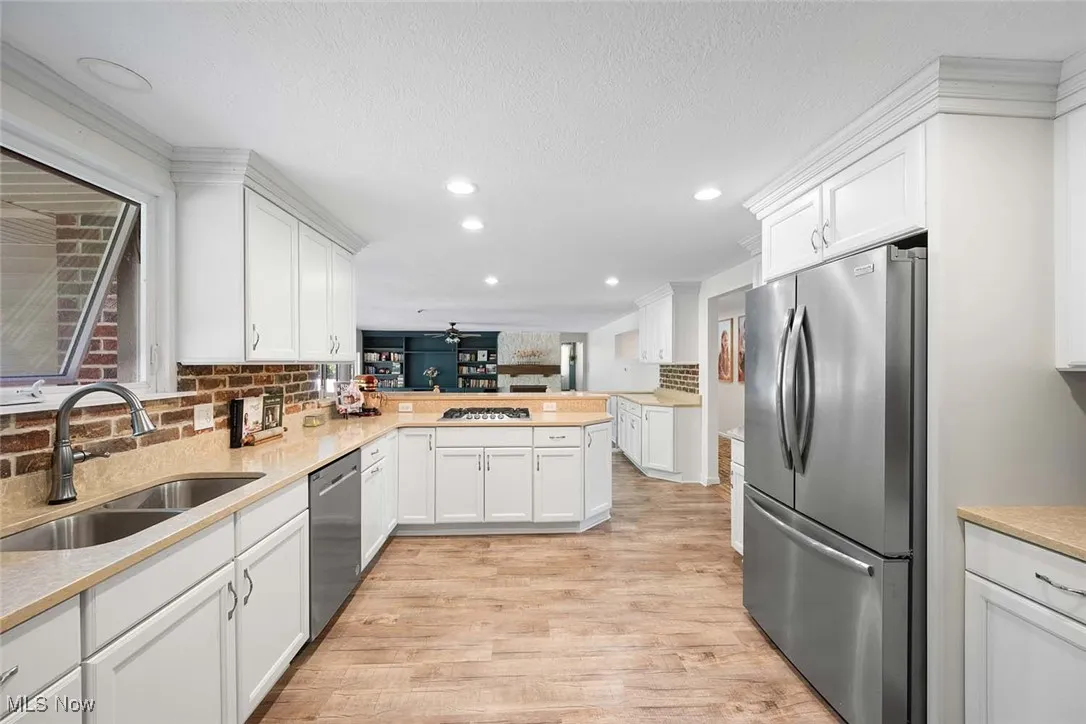 Kitchen with appliances with stainless steel finishes, light wood-style floors, white cabinetry, a peninsula, and tasteful backsplash