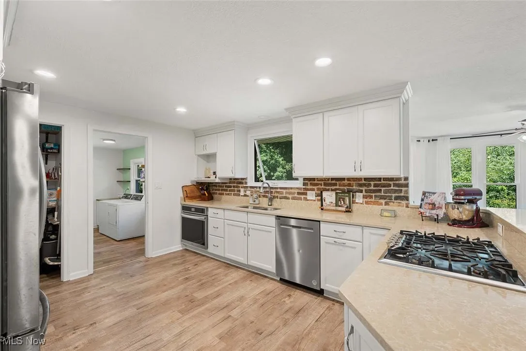 Kitchen featuring stainless steel appliances, light wood-style floors, light countertops, white cabinetry, and washer and clothes dryer