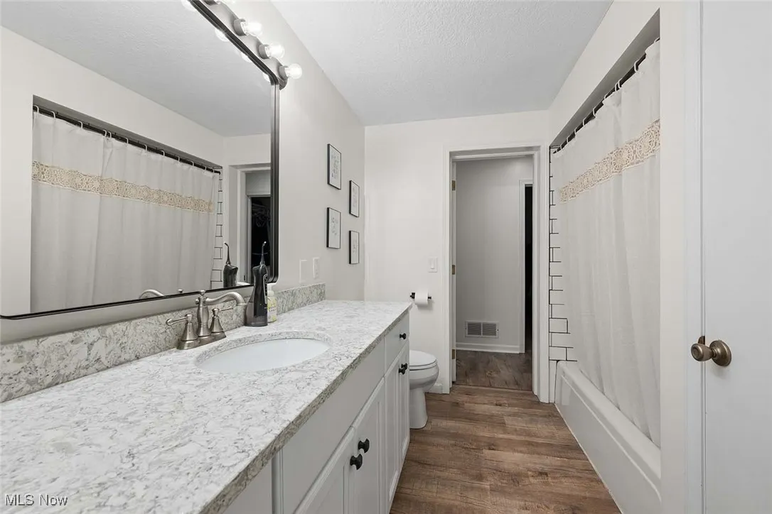 Bathroom with vanity, wood finished floors, a textured ceiling, and shower / bath combo with shower curtain