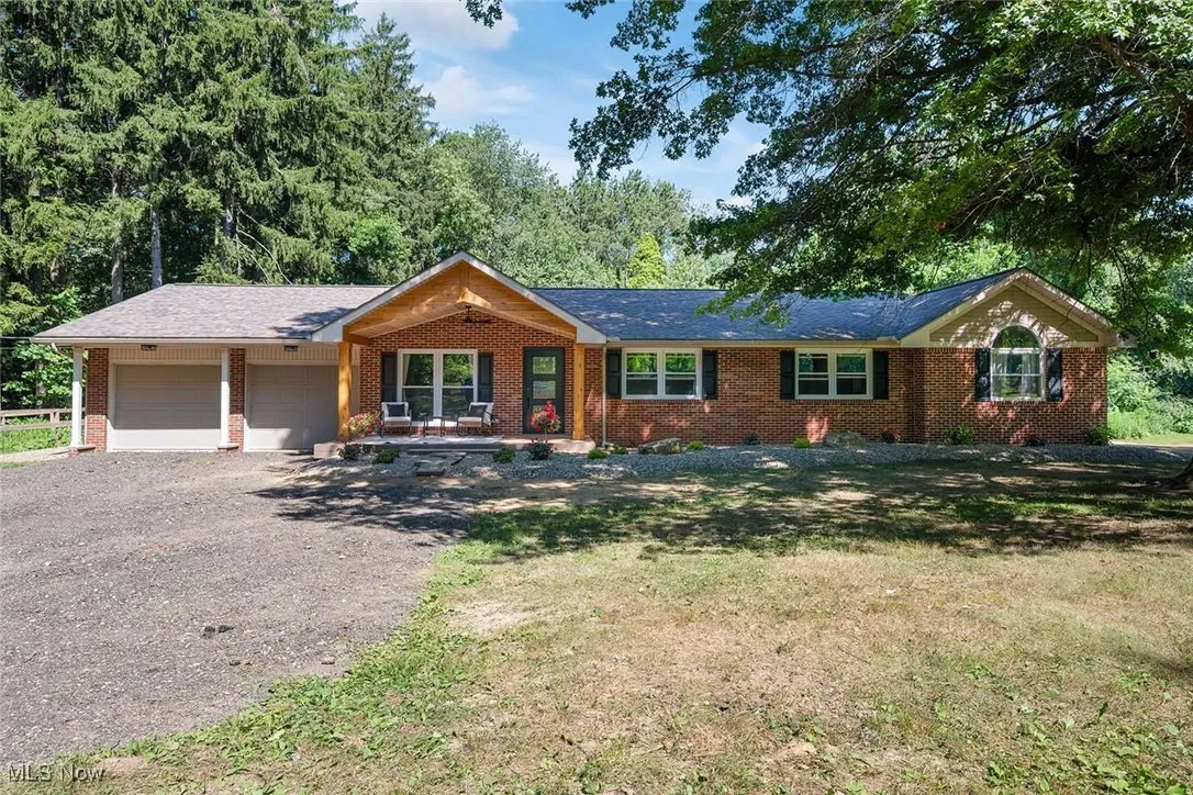 Single story home with gravel driveway, an attached garage, a front lawn, and brick siding