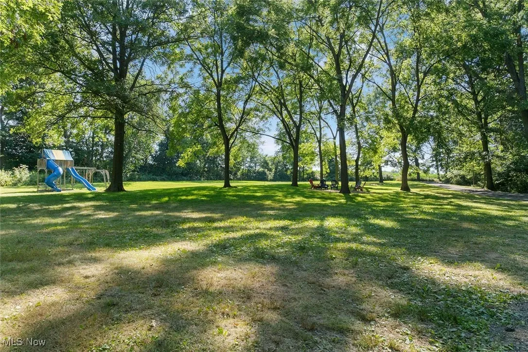 View of grassy yard featuring a playground and view of scattered trees