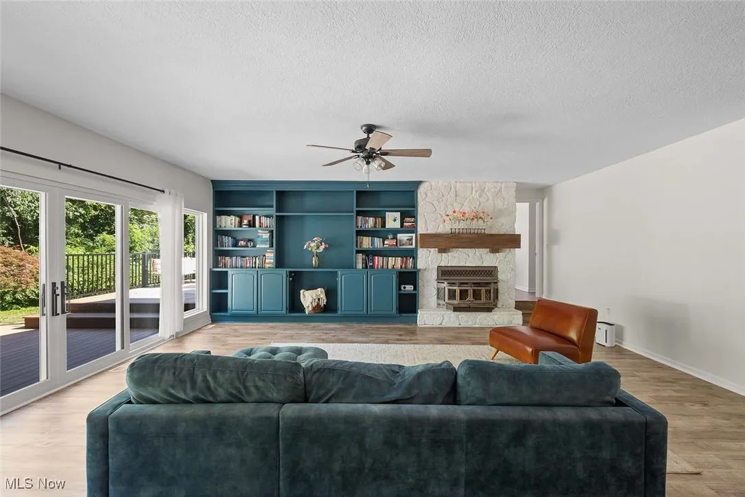 Living area featuring a ceiling fan, light wood-style flooring, a stone fireplace, a textured ceiling, and built in shelves
