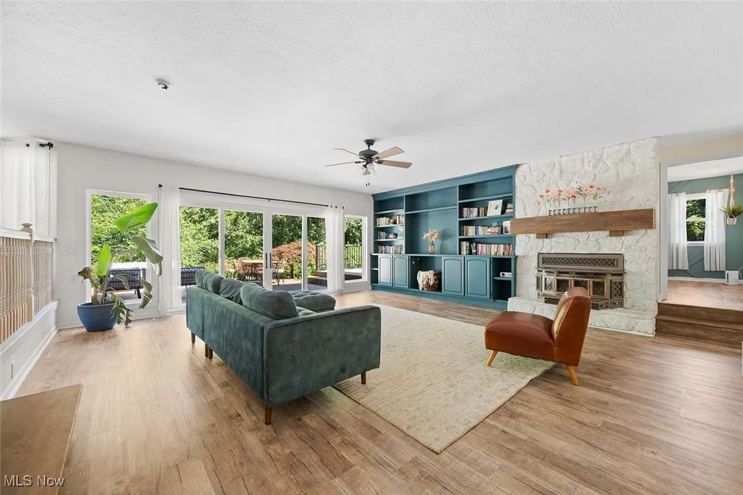 Living room with a ceiling fan, a textured ceiling, wood finished floors, built in shelves, and a fireplace