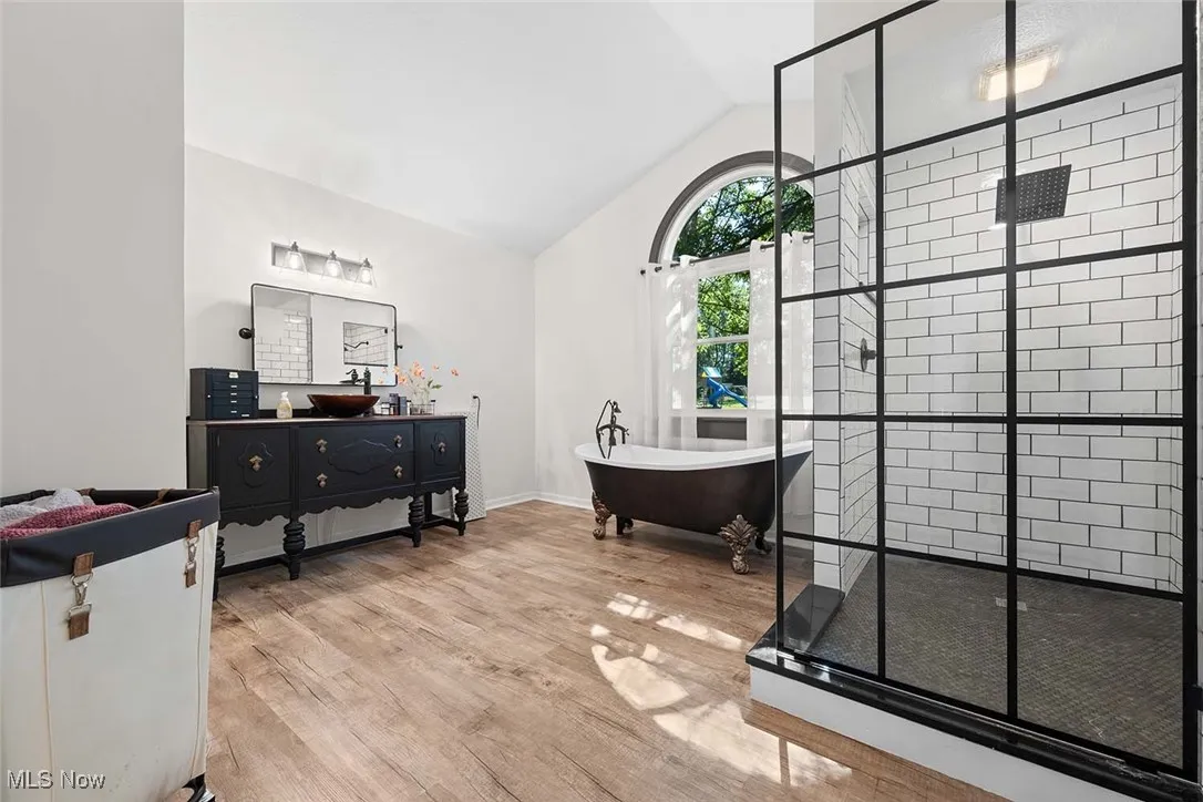 Full bathroom with a stall shower, vanity, lofted ceiling, a soaking tub, and wood finished floors