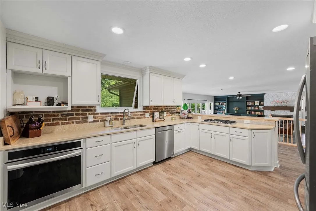 Kitchen with stainless steel appliances, a peninsula, light wood-style floors, a ceiling fan, and light countertops