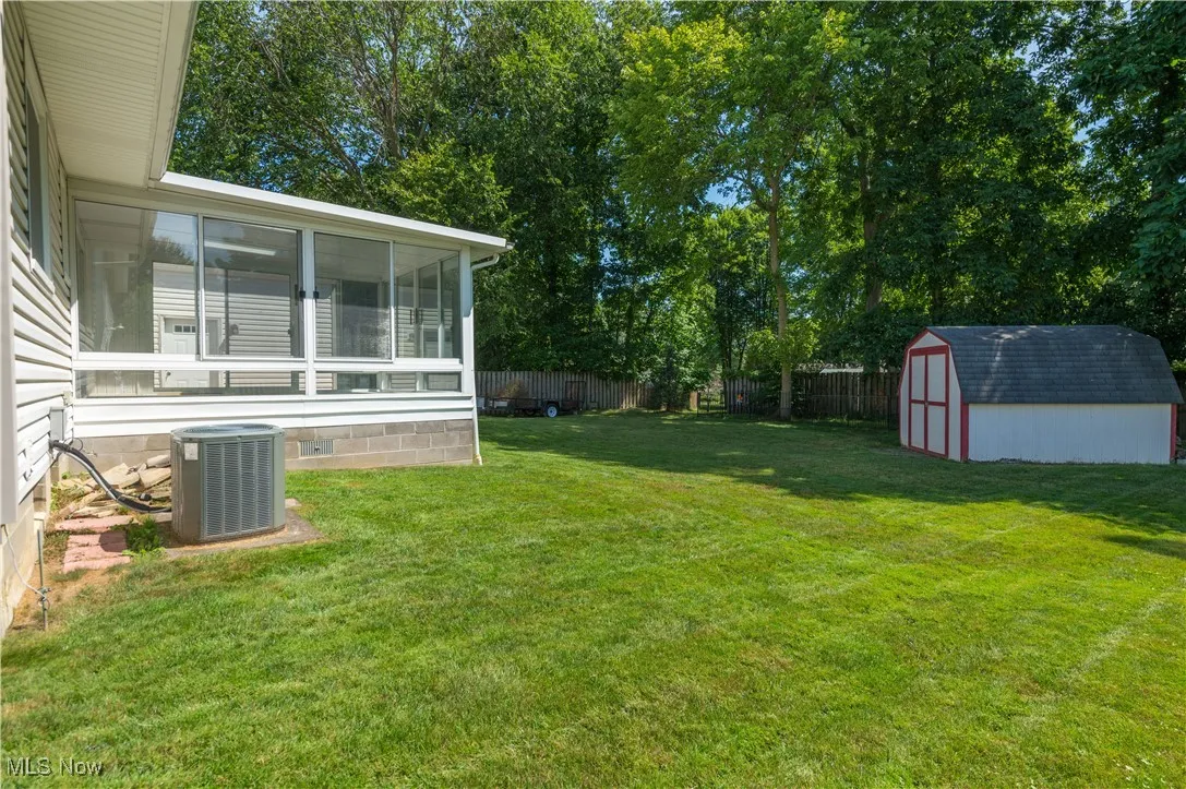 Fenced backyard featuring a sunroom, a shed, and view of scattered trees