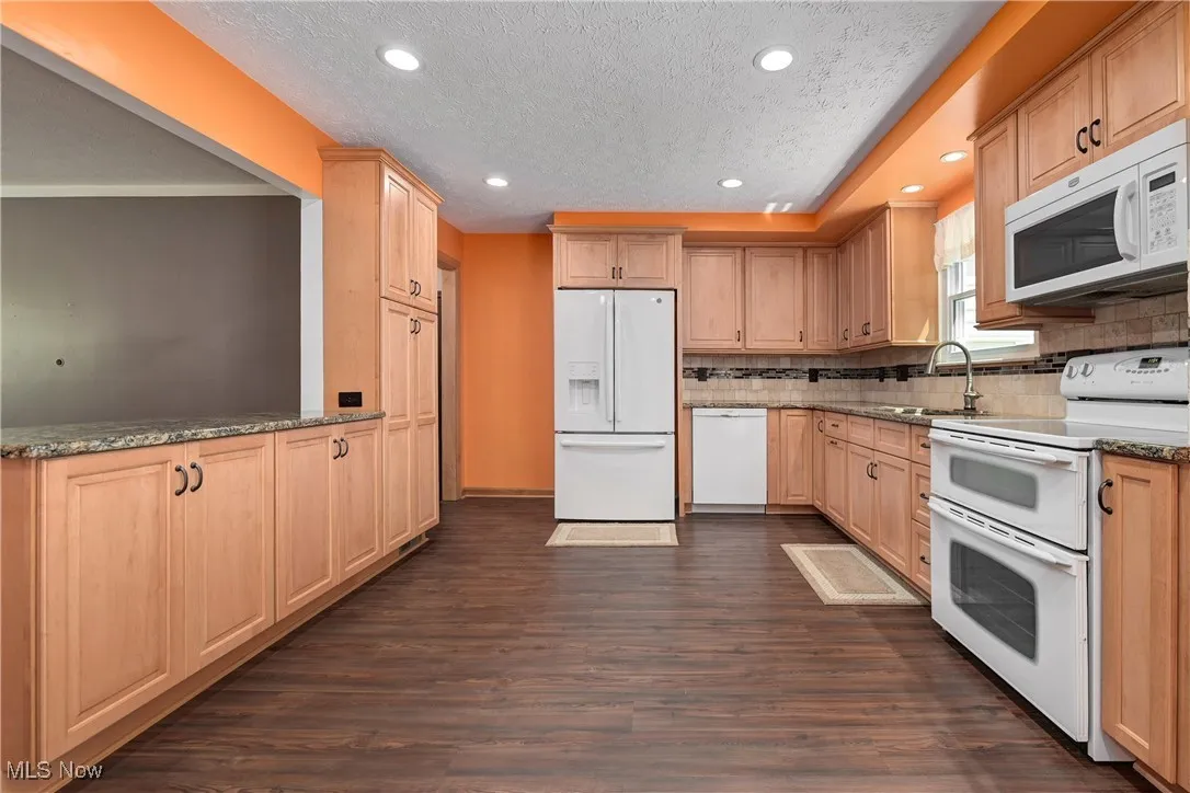 Kitchen with white appliances, light brown cabinetry, dark wood-style flooring, tasteful backsplash, and a textured ceiling