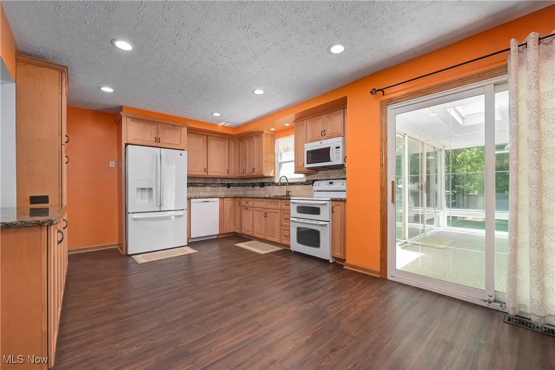 Kitchen with dark wood-type flooring, white appliances, recessed lighting, a textured ceiling, and backsplash