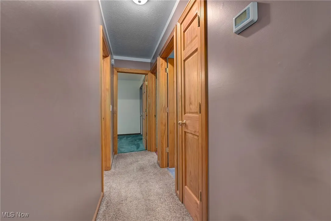 Hallway with light colored carpet and a textured ceiling