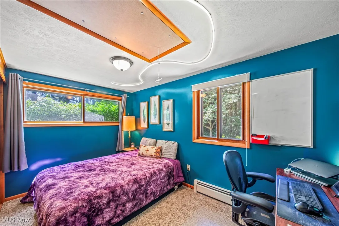 Carpeted bedroom with attic access, a textured ceiling, multiple windows, a baseboard radiator, and an office area