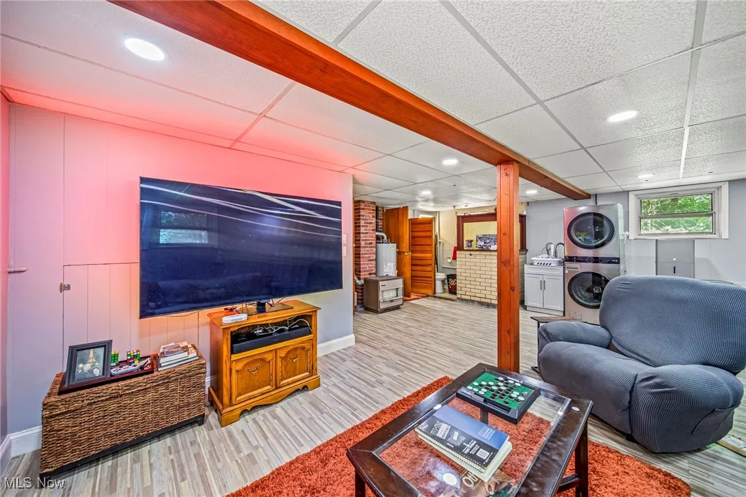 Living area with a paneled ceiling, recessed lighting, stacked washer / drying machine, and wood finished floors