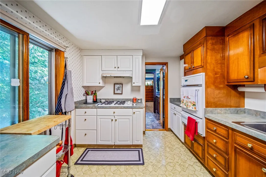 Kitchen with white appliances, white cabinetry, a warming drawer, light flooring, and light countertops