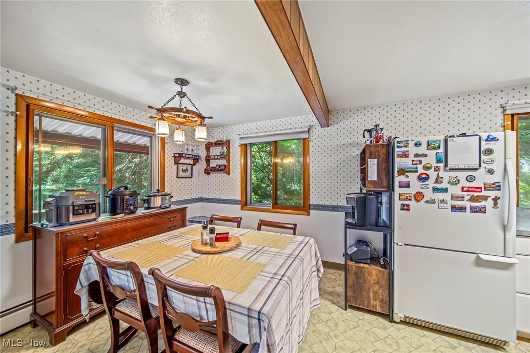 Dining area featuring wallpapered walls, beamed ceiling, light floors, a chandelier, and baseboard heating