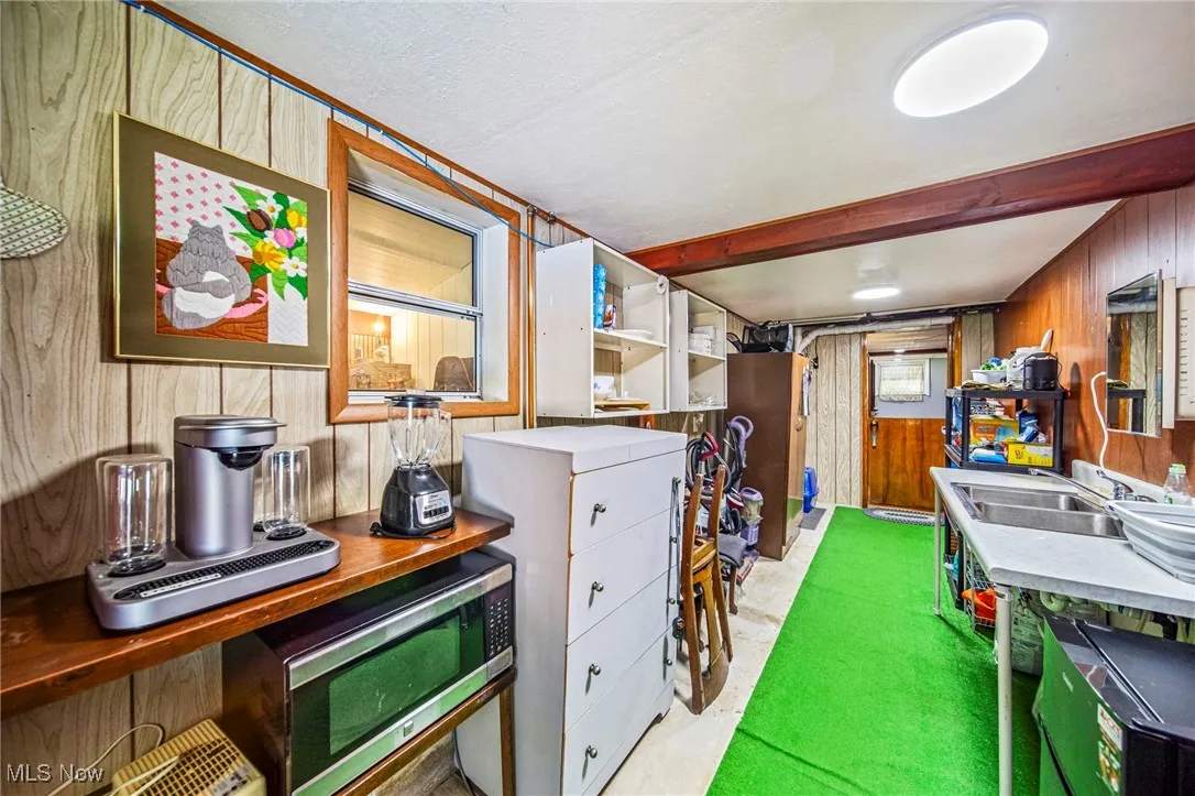 Kitchen with wood walls, stainless steel microwave, beam ceiling, and light countertops