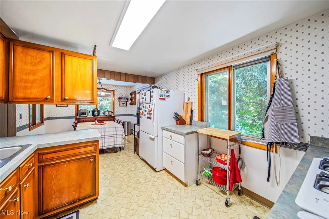 Kitchen with light flooring, white appliances, wallpapered walls, light countertops, and brown cabinets