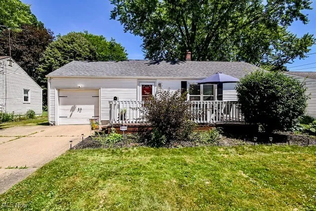 Single story home featuring concrete driveway, a garage, a front lawn, a chimney, and a deck
