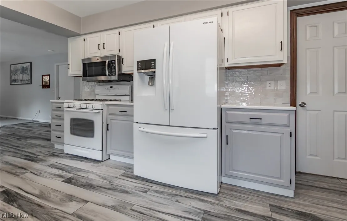 Kitchen featuring white appliances, tasteful backsplash, light countertops, and light wood-type flooring