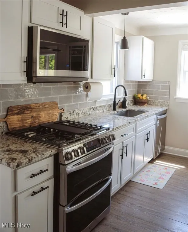 Kitchen with backsplash, appliances with stainless steel finishes, dark wood-type flooring, white cabinets, and light stone countertops