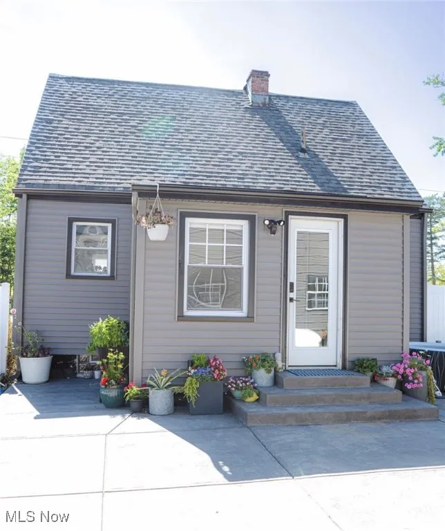 View of front of home with a shingled roof, a chimney, and a patio