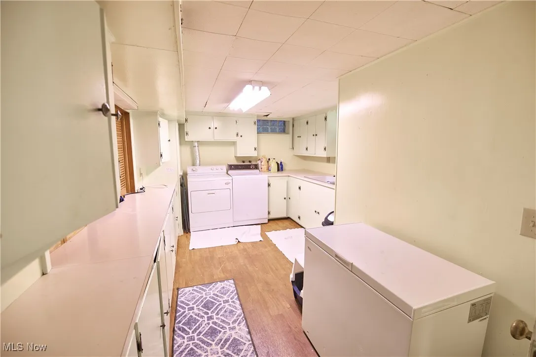 Laundry room with independent washer and dryer, cabinet space, and light wood-style floors