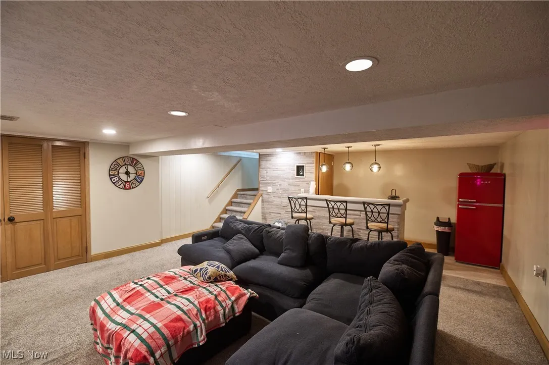 Living room with a textured ceiling, recessed lighting, a bar, carpet, and stairway