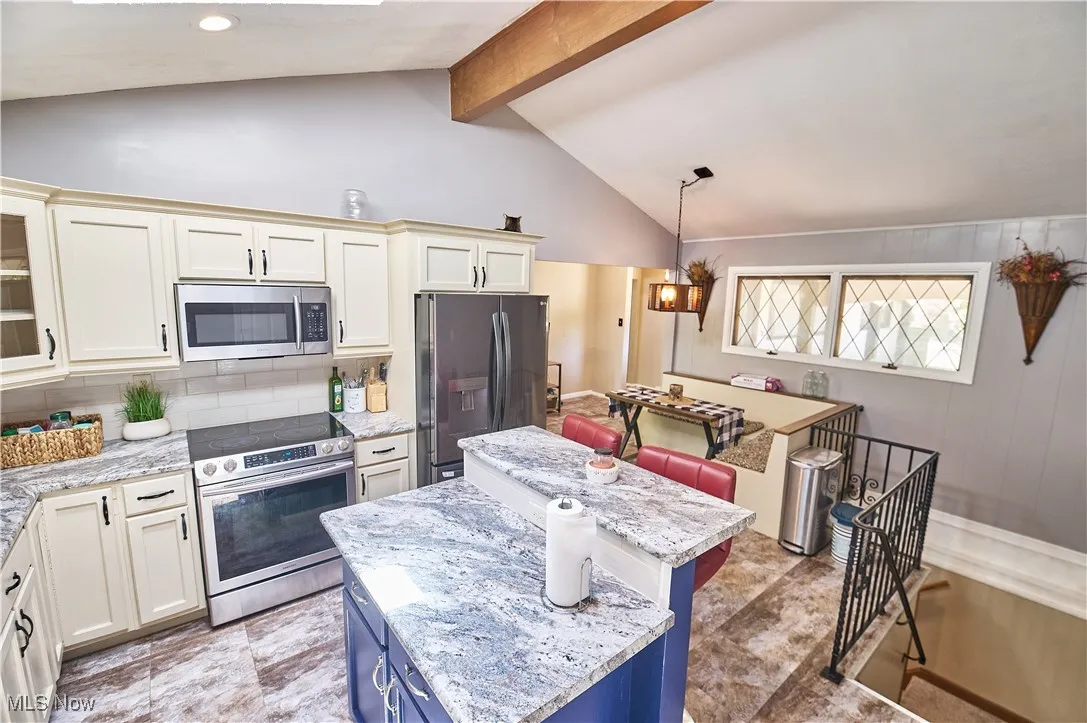 Kitchen with stainless steel appliances, a kitchen island, beam ceiling, tasteful backsplash, and hanging light fixtures