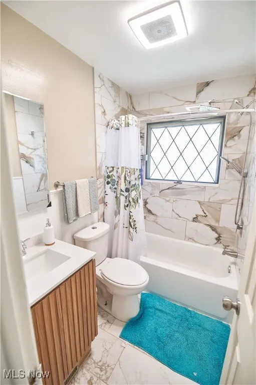 Bathroom with shower / bath combo, vanity, and marble look tile flooring