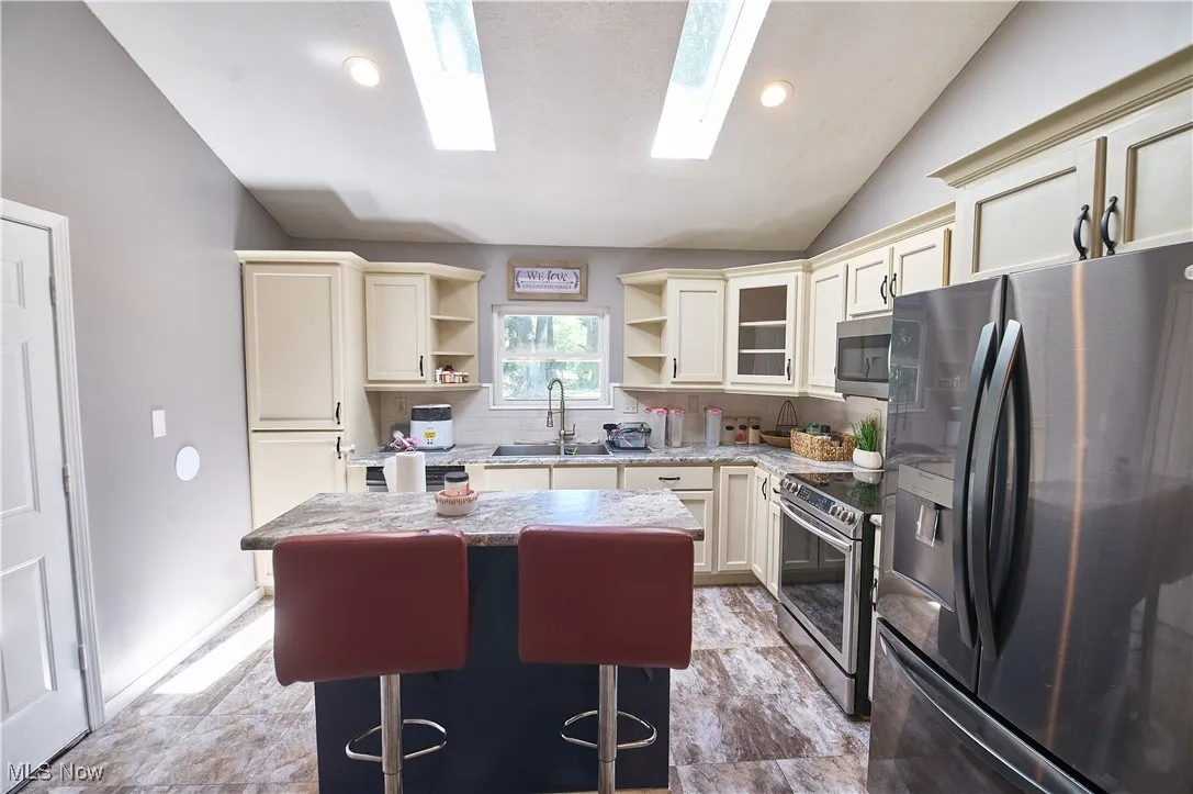 Kitchen with appliances with stainless steel finishes, open shelves, tasteful backsplash, a kitchen island, and lofted ceiling