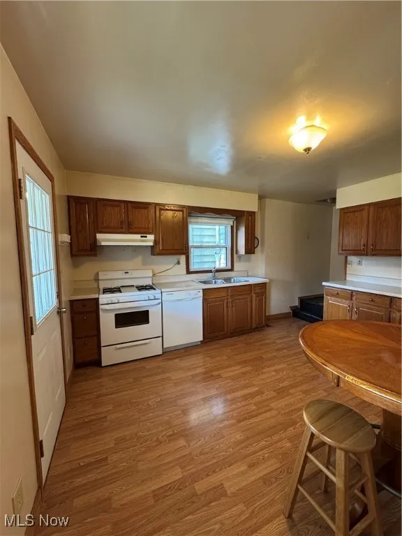 Kitchen with range, wood finished floors, light countertops, dishwashing machine, and exhaust hood