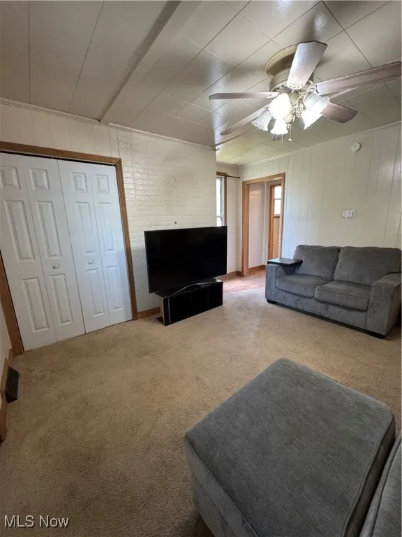 Living area with carpet floors, ceiling fan, and wooden walls