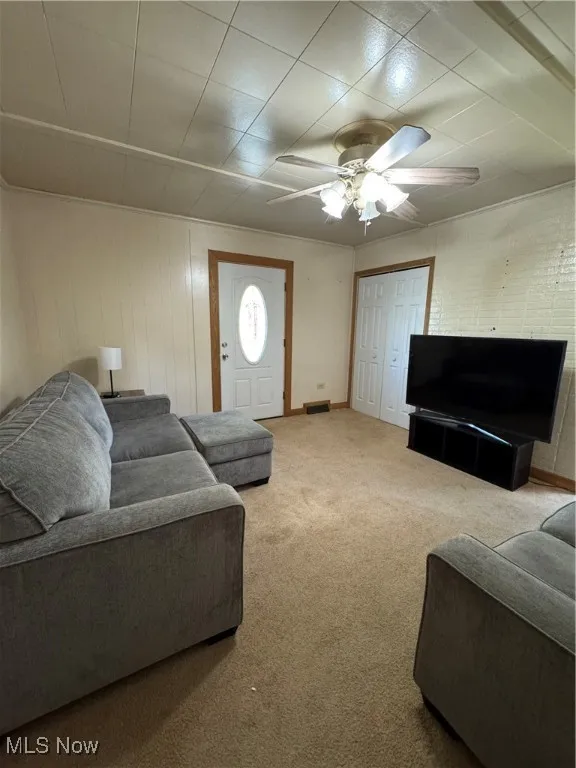 Carpeted living room featuring ceiling fan and baseboards