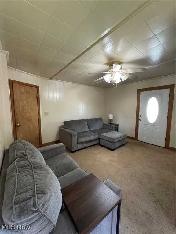 Carpeted living area featuring ceiling fan and baseboards