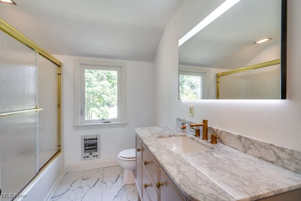 Full bathroom featuring lofted ceiling, vanity, marble look tile flooring, enclosed tub / shower combo, and heating unit