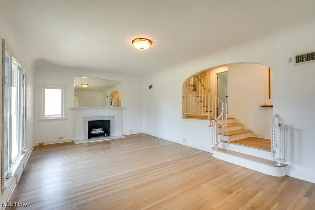 Unfurnished living room with wood finished floors, stairs, a fireplace, and arched walkways