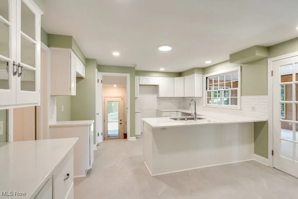 Kitchen with a peninsula, decorative backsplash, glass insert cabinets, white cabinets, and recessed lighting