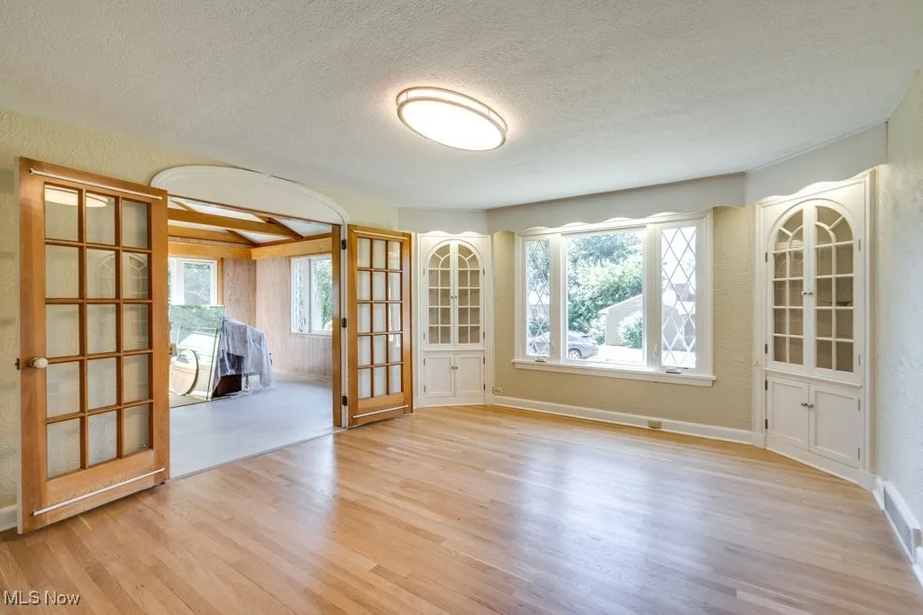 Unfurnished room featuring wood finished floors, a textured ceiling, french doors, and a textured wall