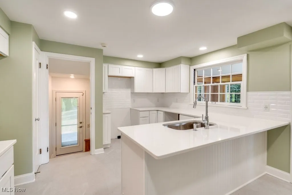 Kitchen with a peninsula, tasteful backsplash, white cabinetry, light countertops, and recessed lighting