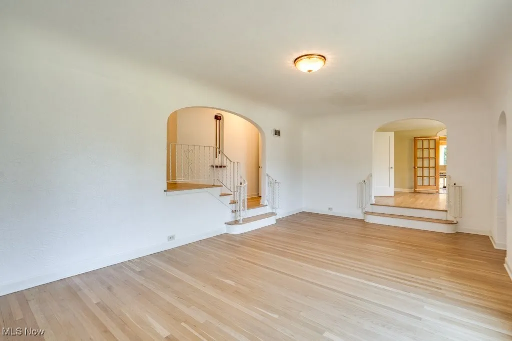 Spare room with stairway, arched walkways, and light wood-style floors