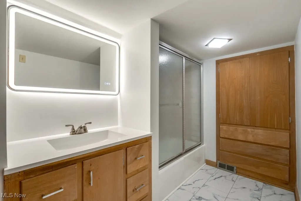 Bathroom featuring vanity, marble look tile flooring, and bath / shower combo with glass door