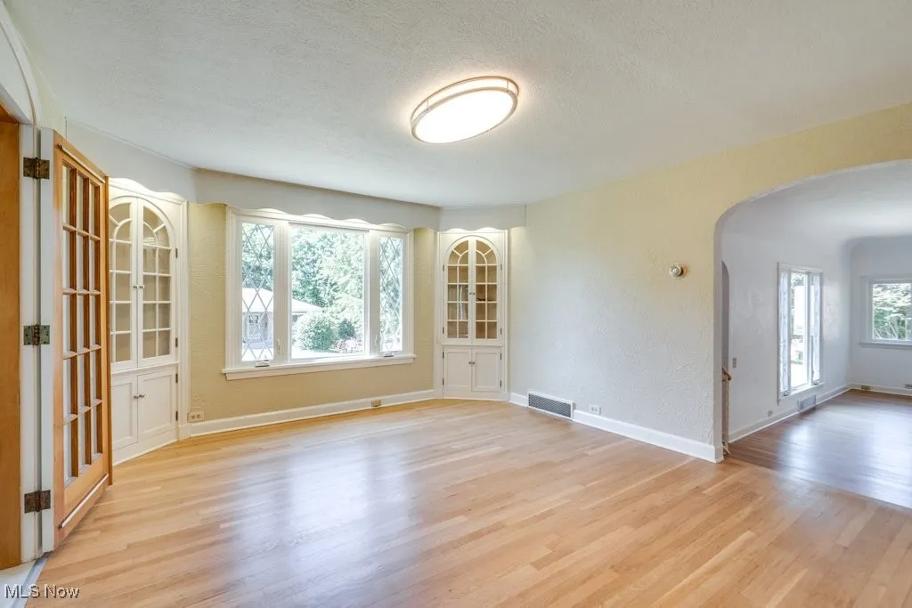Unfurnished room featuring arched walkways, light wood-type flooring, a textured ceiling, and a textured wall