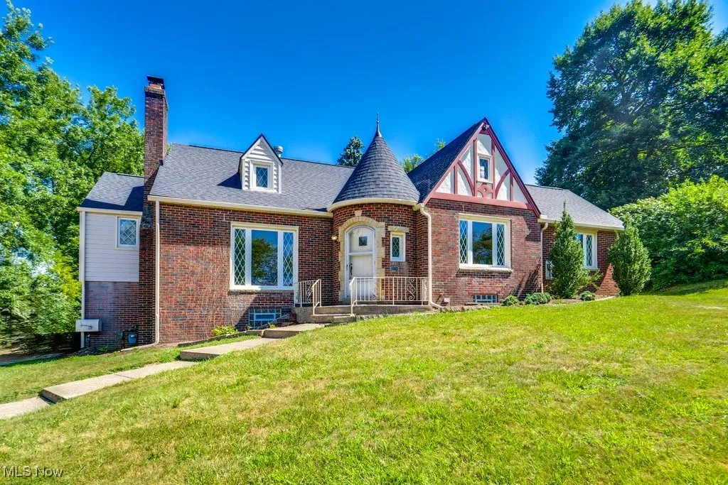 Tudor house with brick siding, a chimney, a front lawn, and a shingled roof