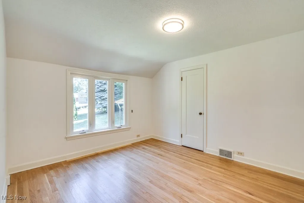Unfurnished room featuring lofted ceiling, wood finished floors, and a textured ceiling