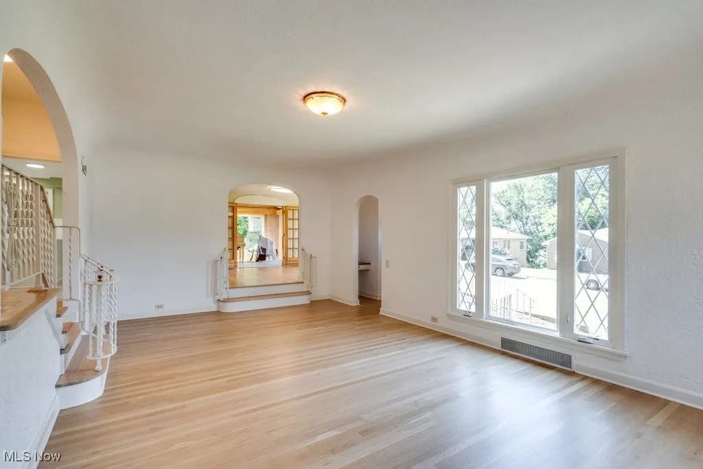 Unfurnished living room with arched walkways, stairway, and light wood finished floors